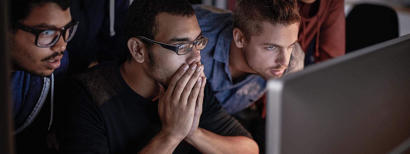 Vier junge Kollegen schauen auf einen PC und versuchen ein Problem zu lösen. 