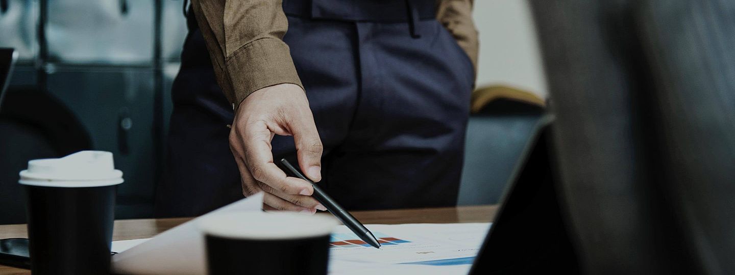 Hand im Business-Meeting zeigt mit Stift auf Papier